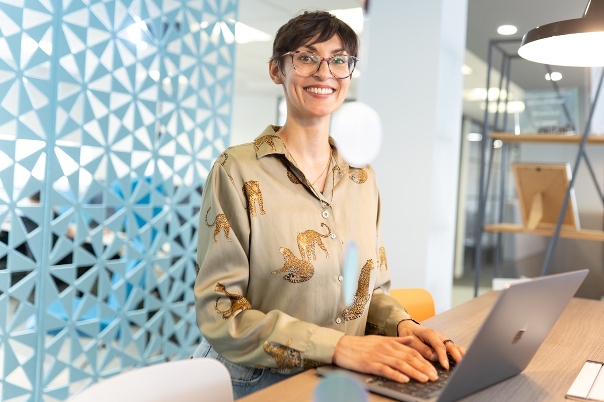 A cheerful colleague works on their laptop in a bright office environment