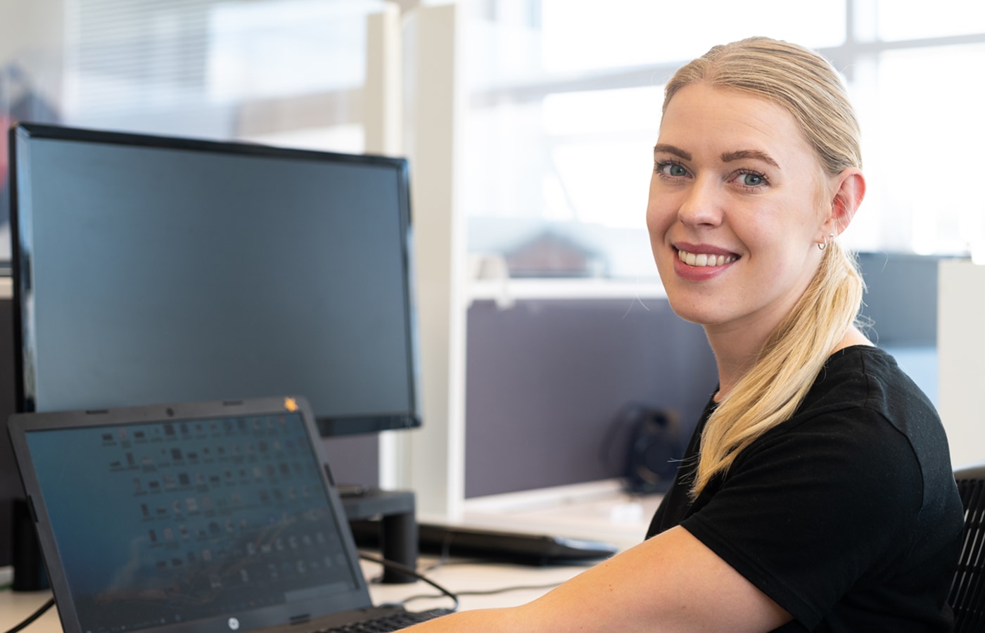 A friendly colleague smiles at the camera whilst working on their laptop